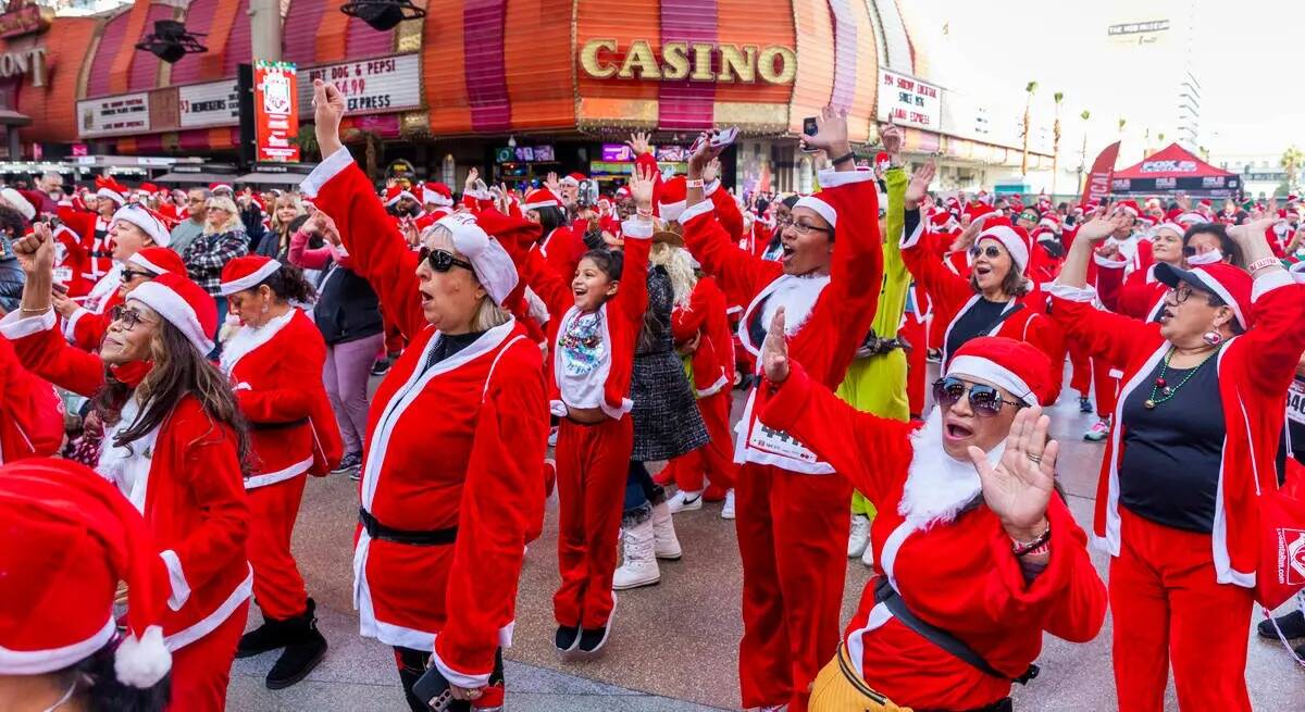 Participantes vestidos con trajes de Santa cantan y bailan durante el entretenimiento previo a ...