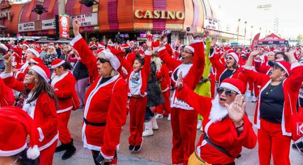 Participantes vestidos con trajes de Santa cantan y bailan durante el entretenimiento previo a ...