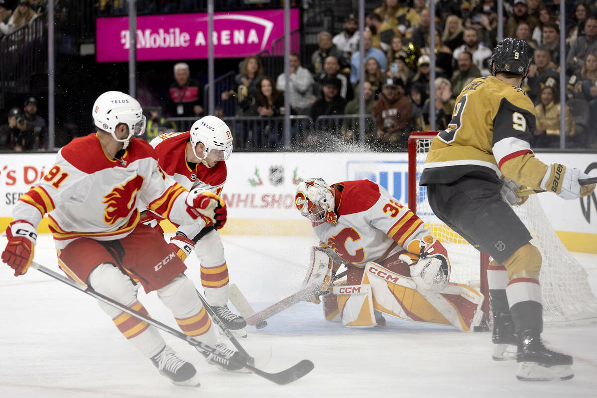 El portero de los Flames Dustin Wolf (32) detiene el puck después de que el centro de los Gold ...