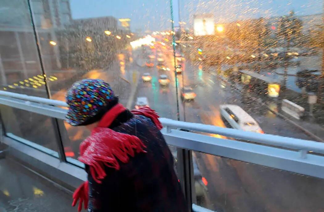 Una mujer abrigada hace frente a la lluvia helada y la nieve mientras cruza uno de los puentes ...