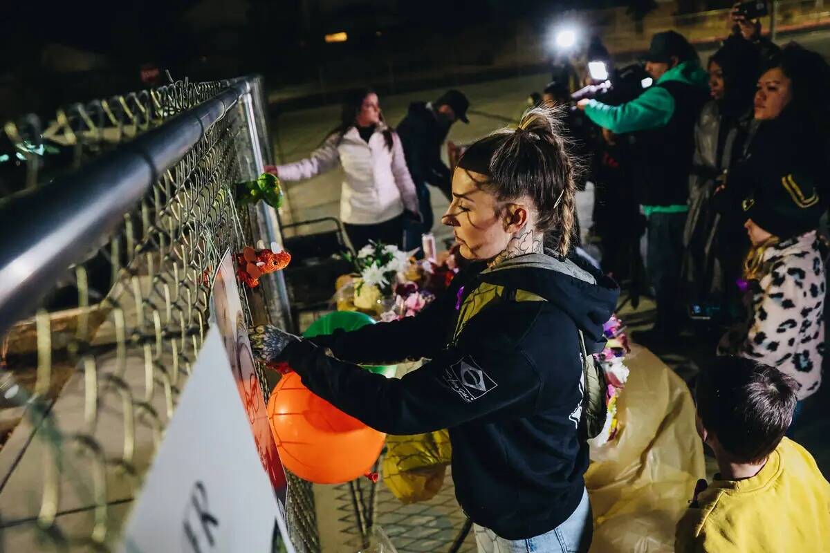 Un doliente ata globos a una valla llena de carteles y fotografías durante una vigilia por Reb ...