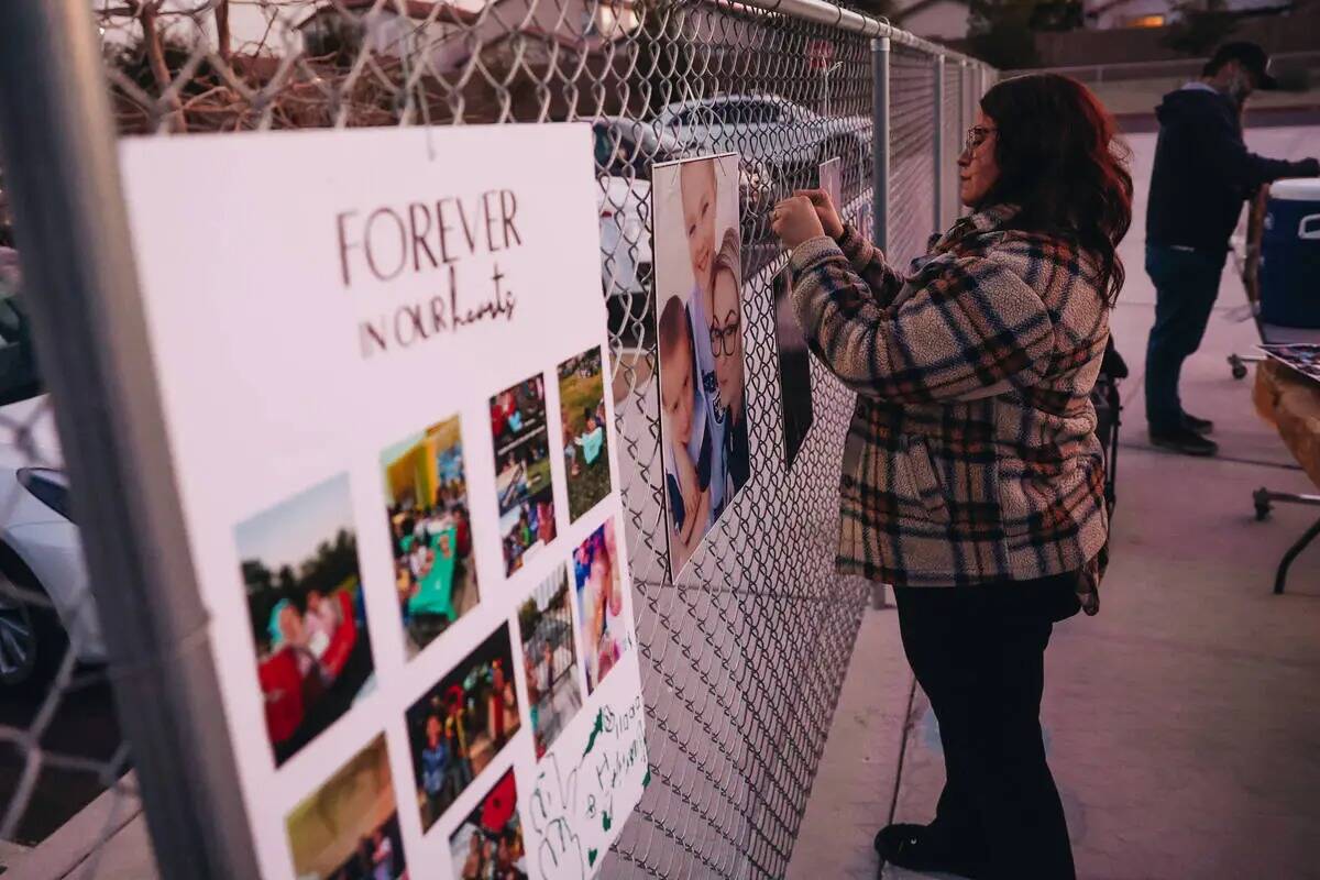 Un doliente toma fotos de carteles y fotografías colgadas en una valla durante una vigilia por ...