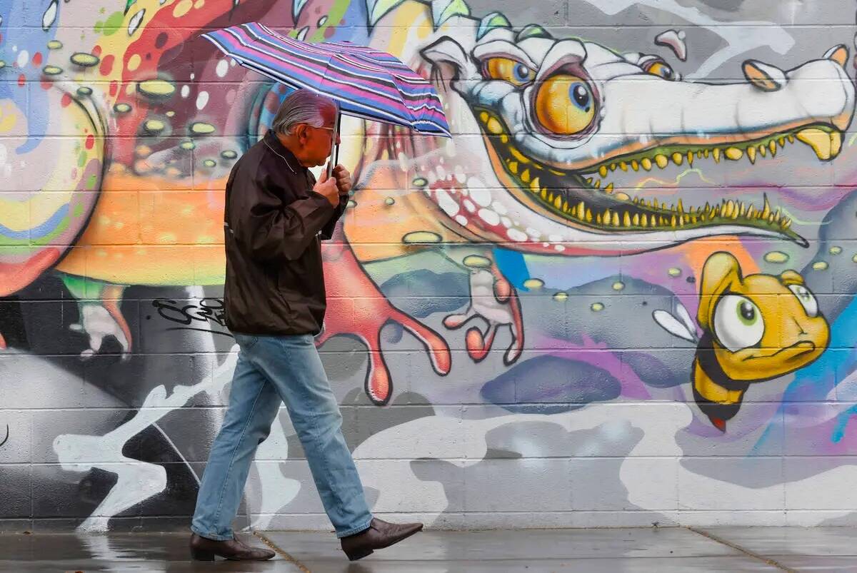 Un peatón con un paraguas pasa por delante de un mural en la Third Street durante una mañana ...