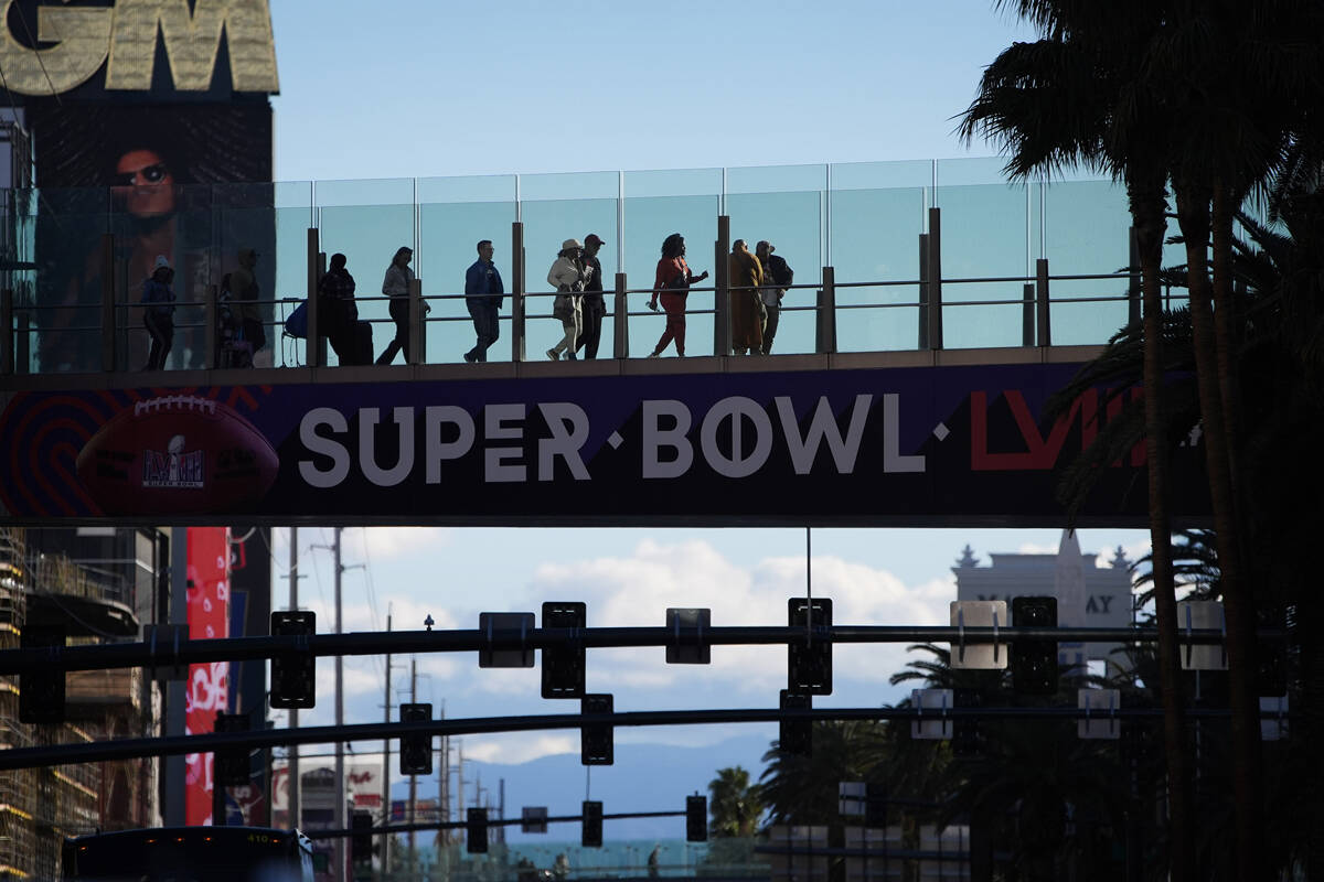 Gente camina por un puente peatonal a lo largo del Strip de Las Vegas antes del Super Bowl 58, ...