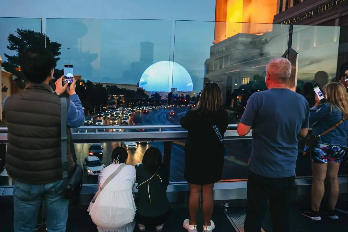 Un grupo de personas deteniéndose en un puente peatonal para tomar fotografías de Sphere, el ...