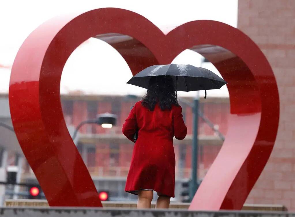 Un peatón bajo un paraguas pasa junto a una escultura de corazón gigante fuera de la Oficina ...