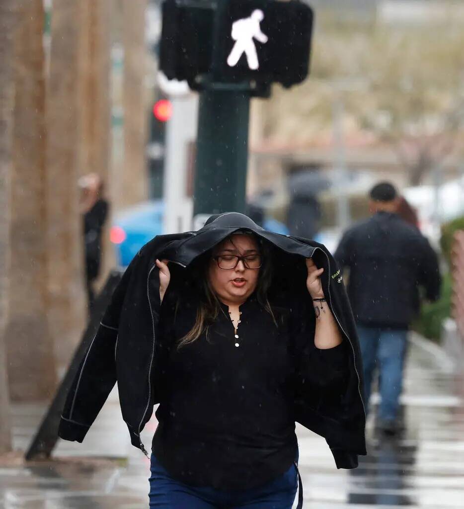 Una peatona se cubre la cabeza bajo su chaqueta mientras camina por Third Street durante una ma ...