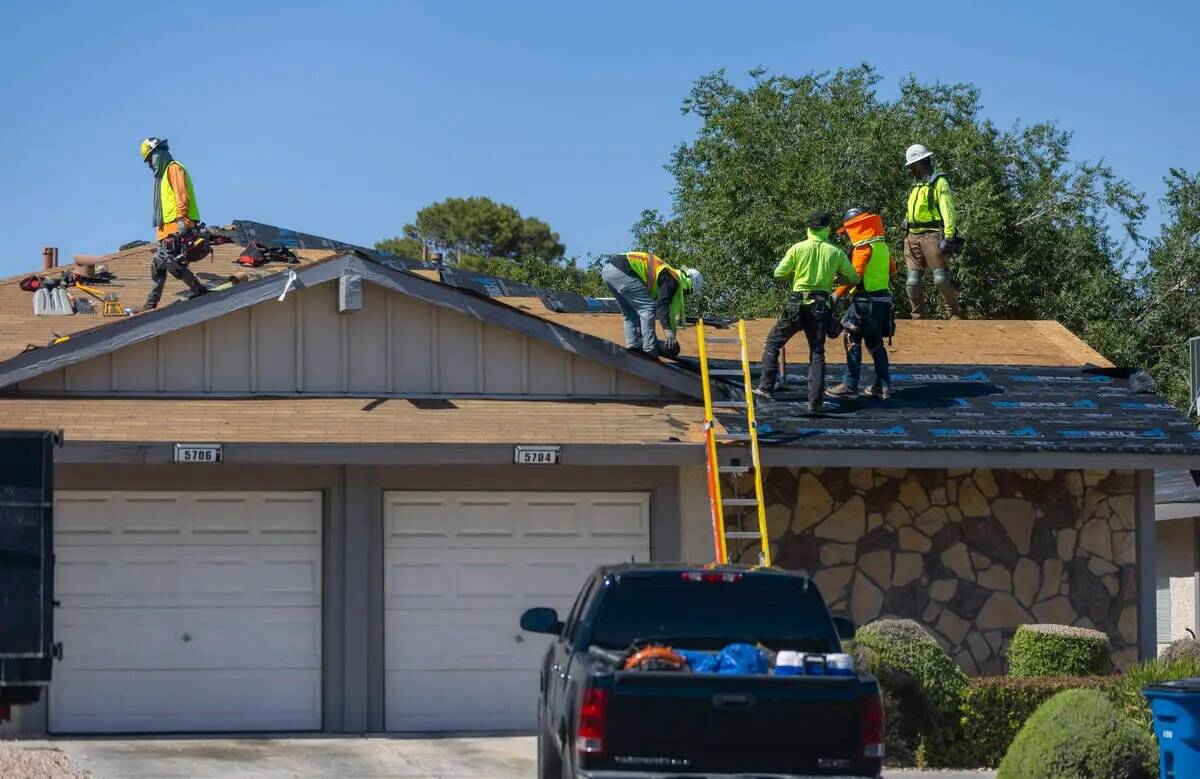 Un equipo trabaja sobre un techo a lo largo de Smoke Ranch Road mientras toman protecciones con ...
