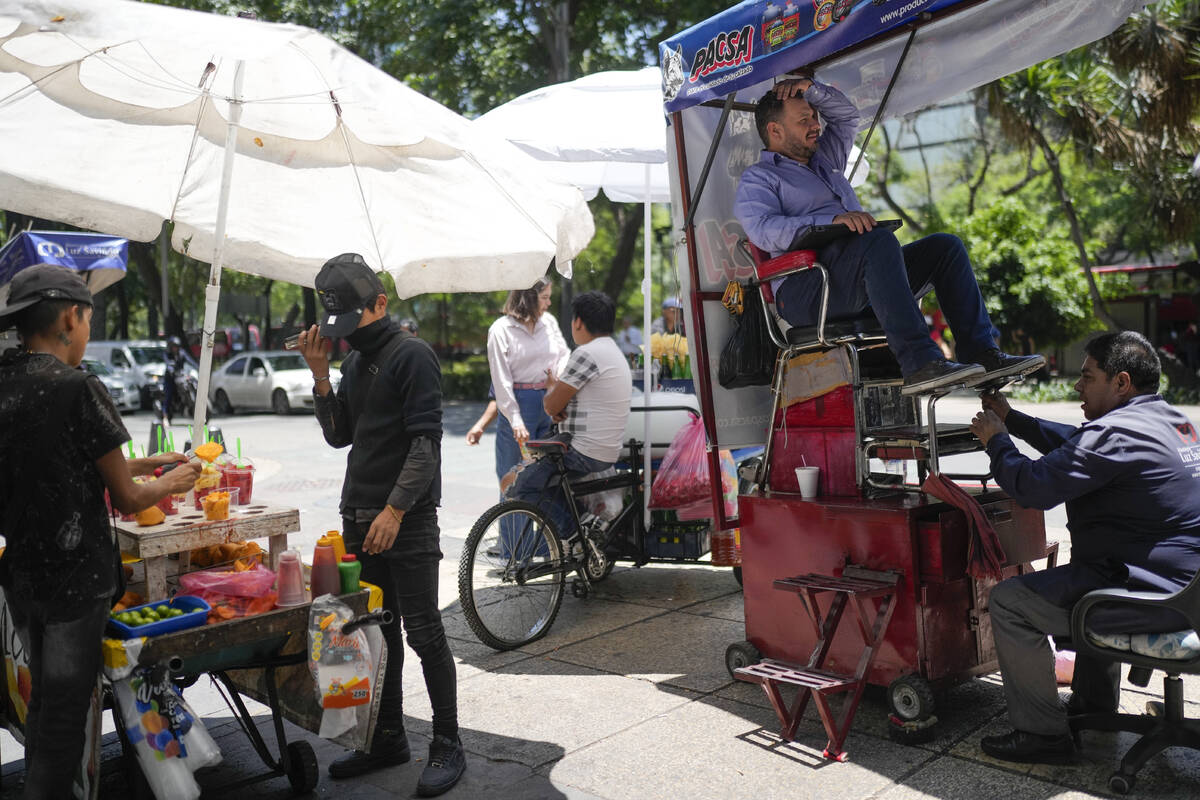 Un lustrabotas y un vendedor de frutas trabajan en la acera en Ciudad de México, el lunes 3 de ...