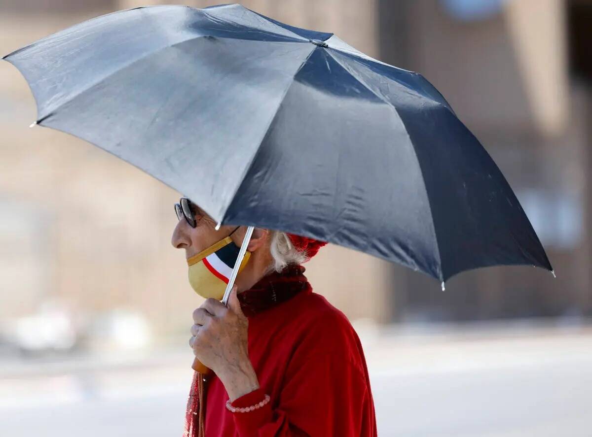 Una mujer sostiene un paraguas para protegerse del sol mientras camina por Main Street, el juev ...