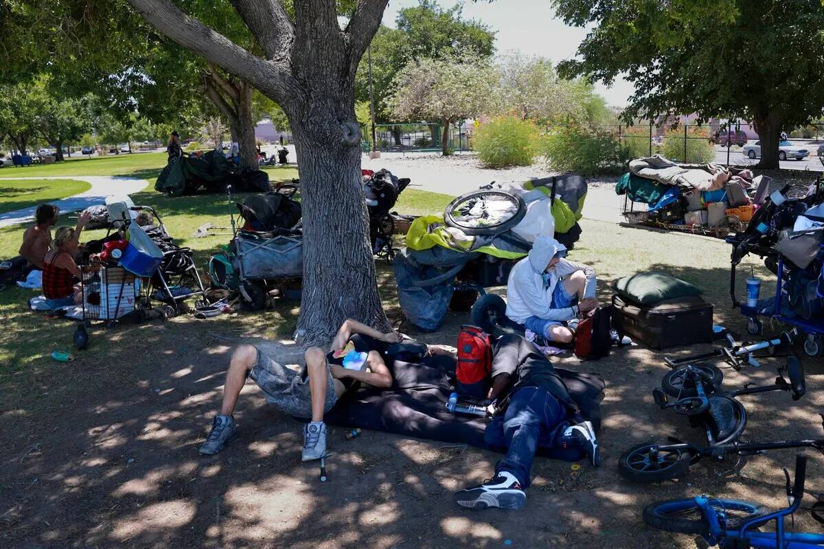 Varias personas se protegen del sol con sus pertenencias en el parque Justice Myron E. Leavitt ...