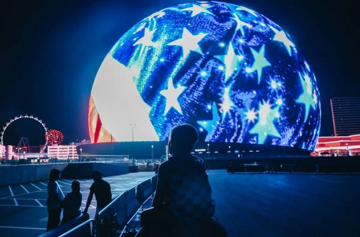 Un niño pequeño se sienta sobre unos hombros mientras observa la Sphere mientras suenan fuego ...