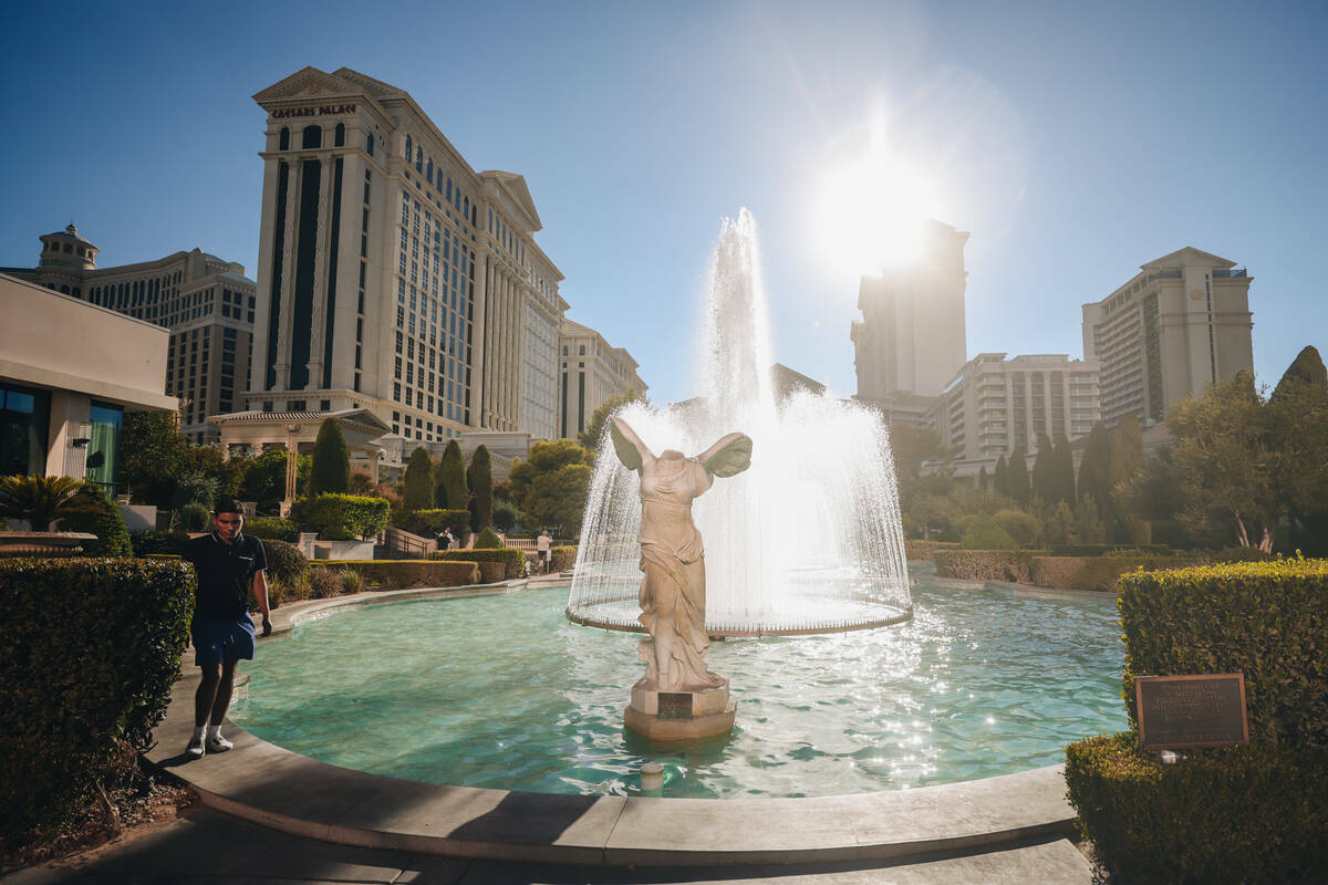 Un turista camina junto a las fuentes del Caesars Palace para mantenerse fresco mientras cae el ...