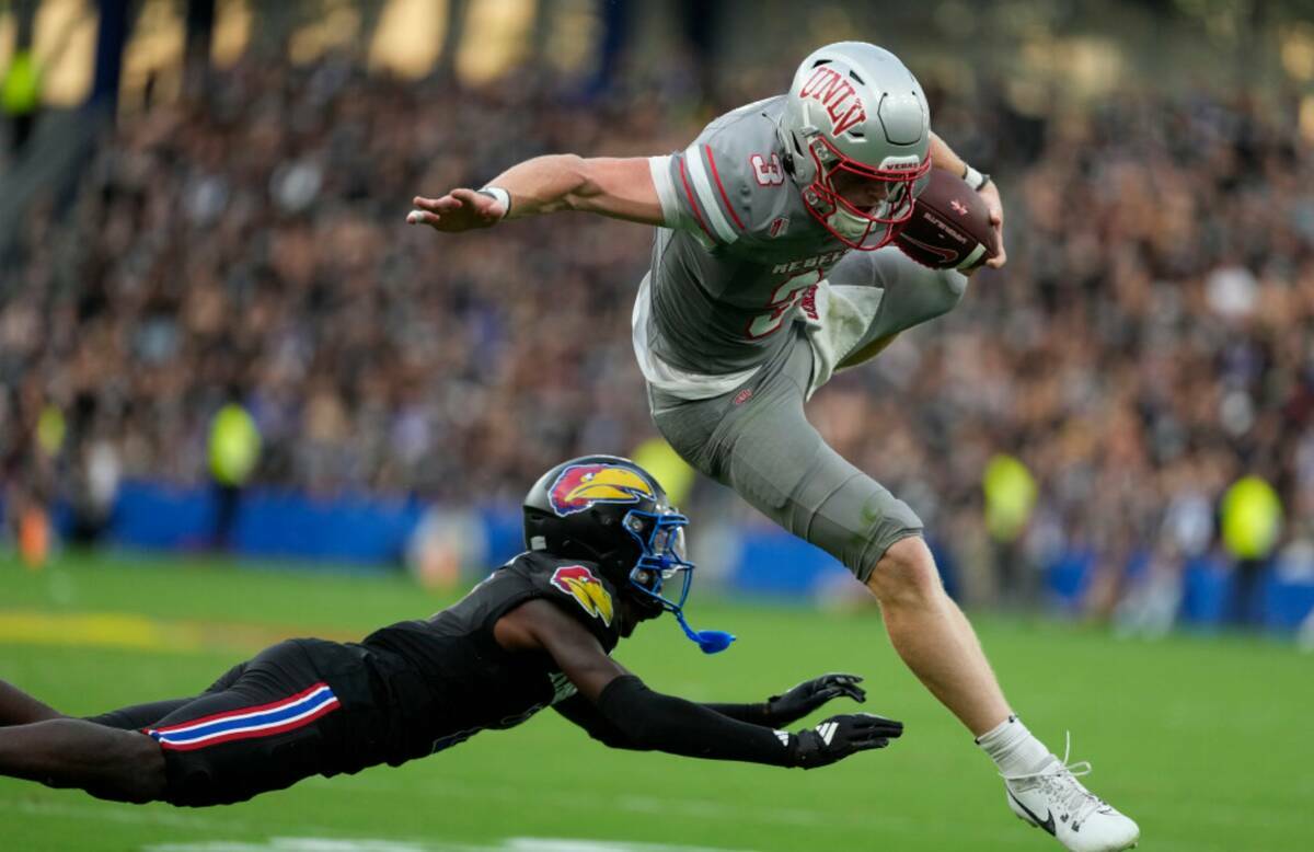 El quarterback de la UNLV Matthew Sluka (3) salta por delante del cornerback de Kansas Cobee Br ...