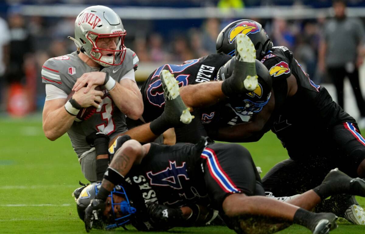 El quarterback de la UNLV Matthew Sluka (3) es atacado por el linebacker de Kansas Cornell Whee ...