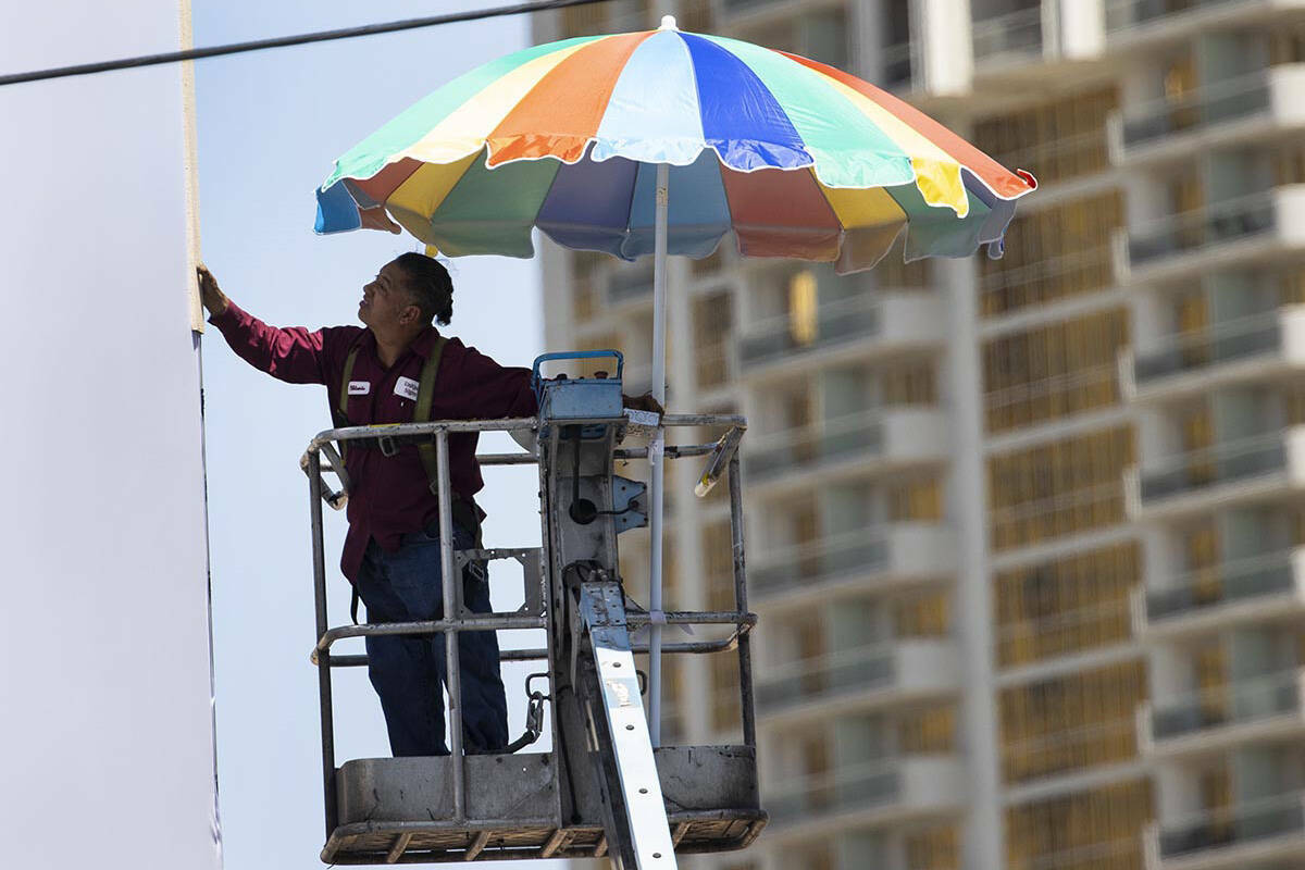 Un trabajador usa una sombrilla gigante para protegerse del sol mientras trabaja en una estruct ...