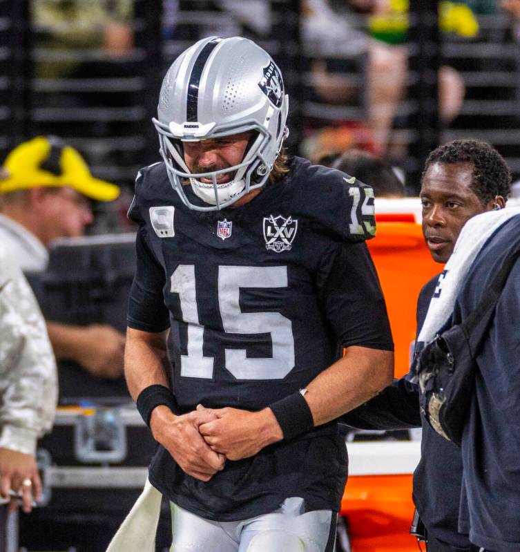 El quarterback de los Raiders Gardner Minshew (15) es escoltado fuera del campo después de un ...